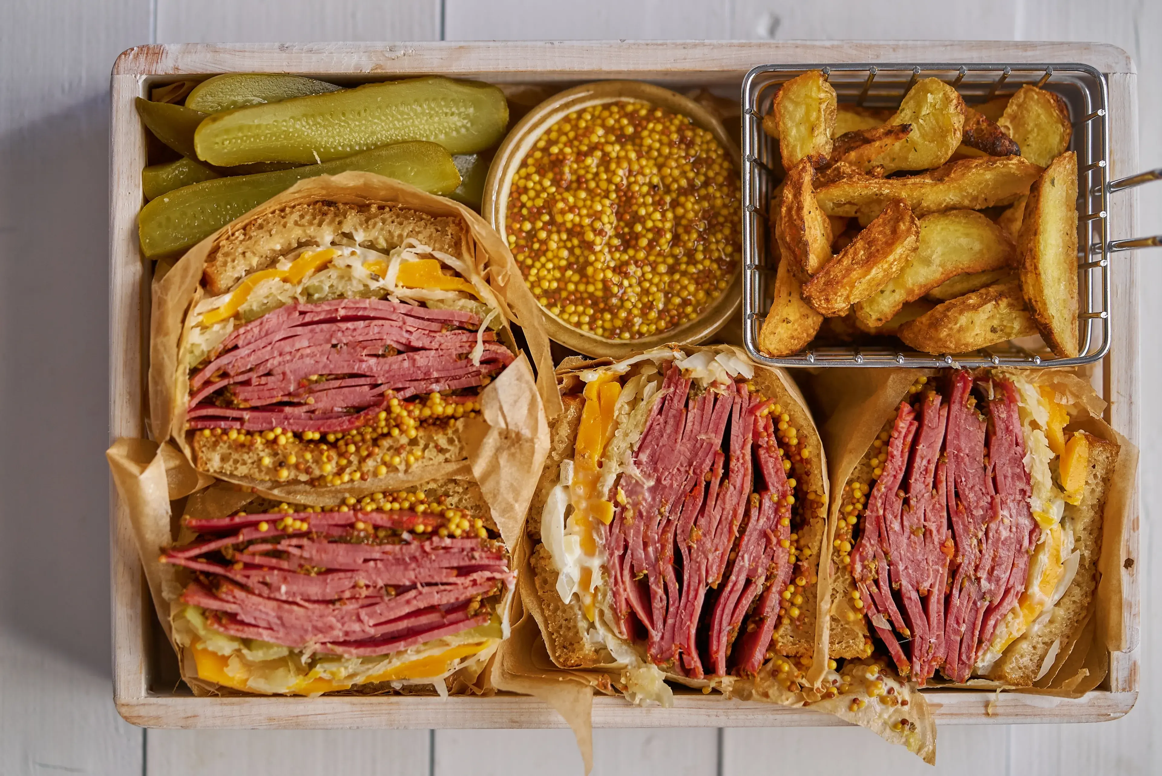Enormous sandwiches with pastrami beef in wooden box. Served with baked potatoes, pickles